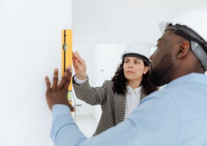 Two contractors using a level tool on a wall indoors