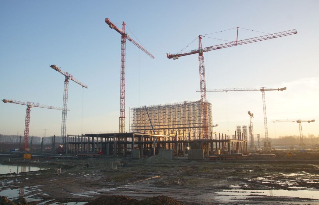 Wide view of a construction site with cranes and building framework at sunset. Industrial landscape.