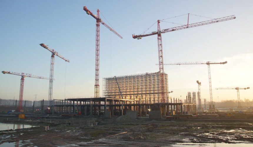 Wide view of a construction site with cranes and building framework at sunset. Industrial landscape.