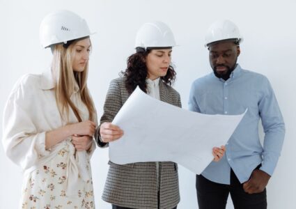 Three architects wearing hard hats reviewing blueprints