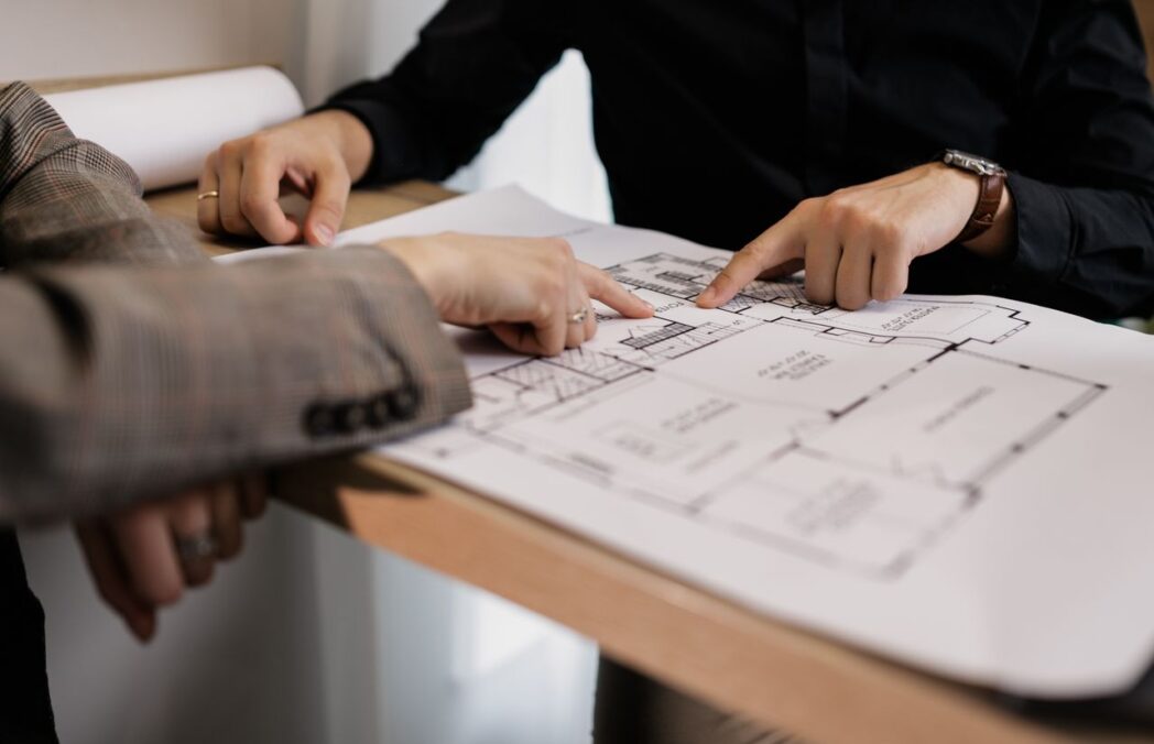 Two architects reviewing and pointing at a detailed floor plan on paper