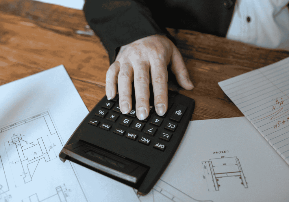 Hand using calculator for architectural calculations on blueprints.