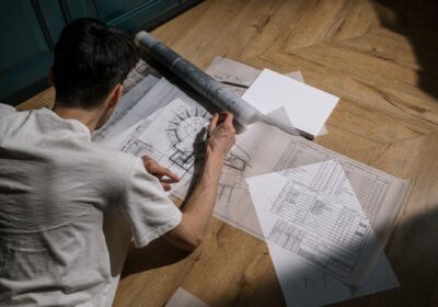 man drawing architectural designs on wooden floor with sunlight streaming