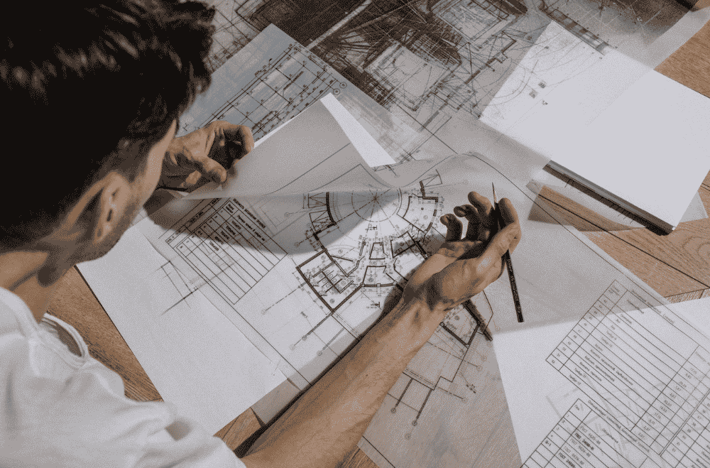 Architect studying and sketching over detailed architectural blueprints indoors.