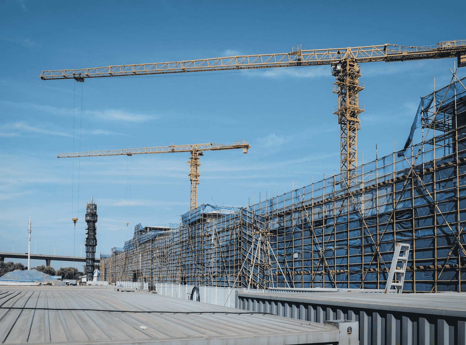 View of a construction site with yellow tower cranes and scaffolding under a clear blue sky.